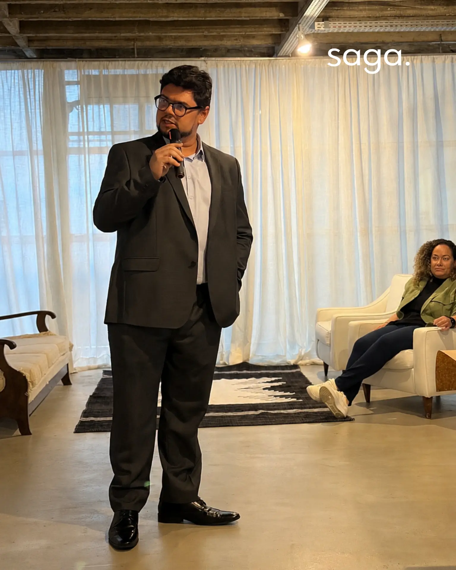 Professor conduzindo uma sessão em pé, com microfone, em ambiente de aprendizagem contemporâneo da SaGa