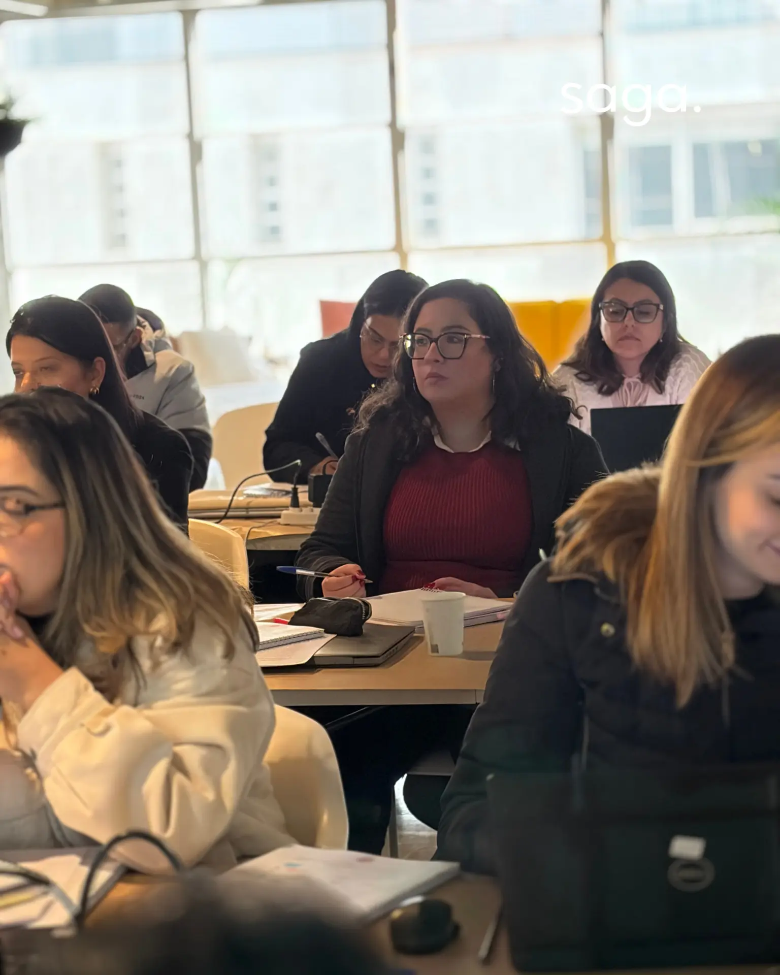 Participante concentrada anotando durante uma sessão do programa, cercada por outros profissionais jurídicos